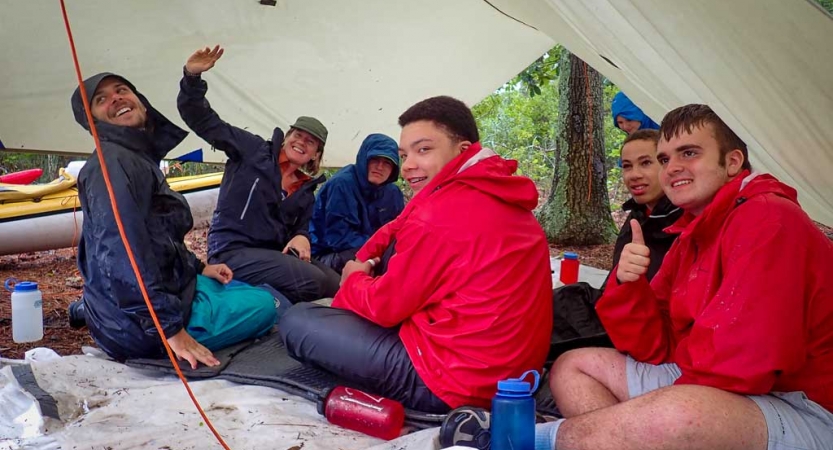 a group of teens rest under a tarp on an outward bound expedition 